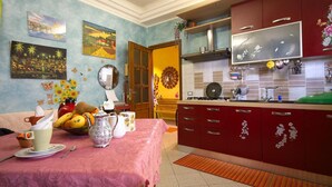 A kitchen with red cabinets, a dining table with a pink tablecloth, and various kitchen appliances. - Casa Arcobaleno (Rome)
