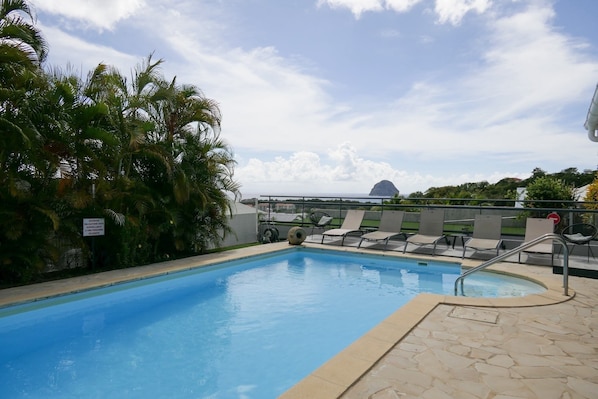 A swimming pool with lounge chairs, palm trees, and a dome structure in the background. - Magnificent villa close to the sea (Le Diamant)