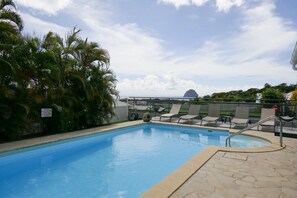 A swimming pool with lounge chairs, palm trees, and a dome structure in the background.