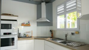 Eine moderne Küche mit weißen Schränken, einer Bosch-Mikrowelle, einem Einbauofen, einer Spüle aus Edelstahl und einem Fenster mit weißen Fensterläden.