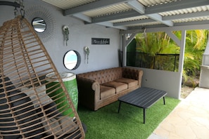 Un espacio al aire libre acogedor con un sofá acolchado, un sillón colgante y una pequeña mesa.