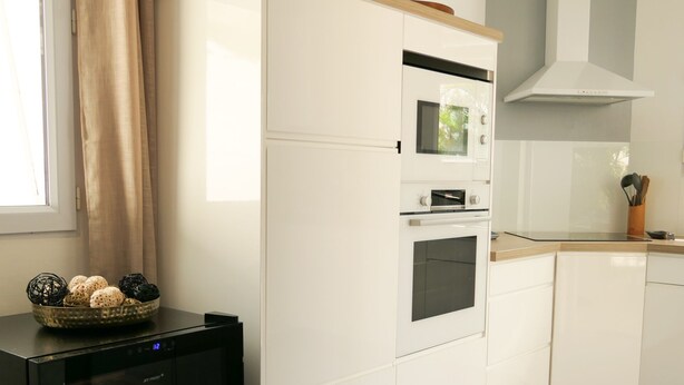 A kitchen with white cabinetry, a built-in oven, and a black appliance with a glass door. - Magnificent villa close to the sea (Le Diamant)