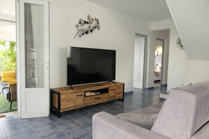 Un salon moderne avec un téléviseur à écran plat posé sur une console en bois, un canapé gris et une porte vitrée donnant sur l’extérieur.