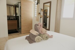 Una cama bien hecha con toallas enrolladas, una puerta de madera, un baño con espejo y una ventana.