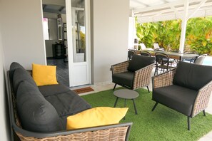A covered outdoor seating area with wicker furniture, a sofa, and a dining table.
