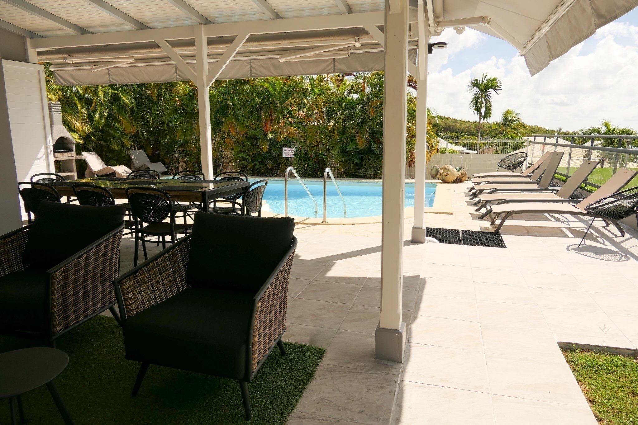A covered outdoor area with a pool, lounge chairs, and wicker furniture.