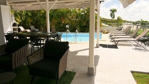 A covered outdoor area with a pool, lounge chairs, and wicker furniture. - Magnificent villa close to the sea (Le Diamant)