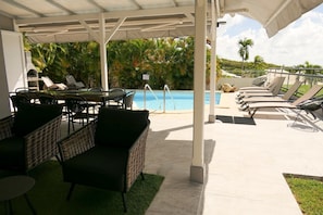 A covered outdoor area with a pool, lounge chairs, and wicker furniture.