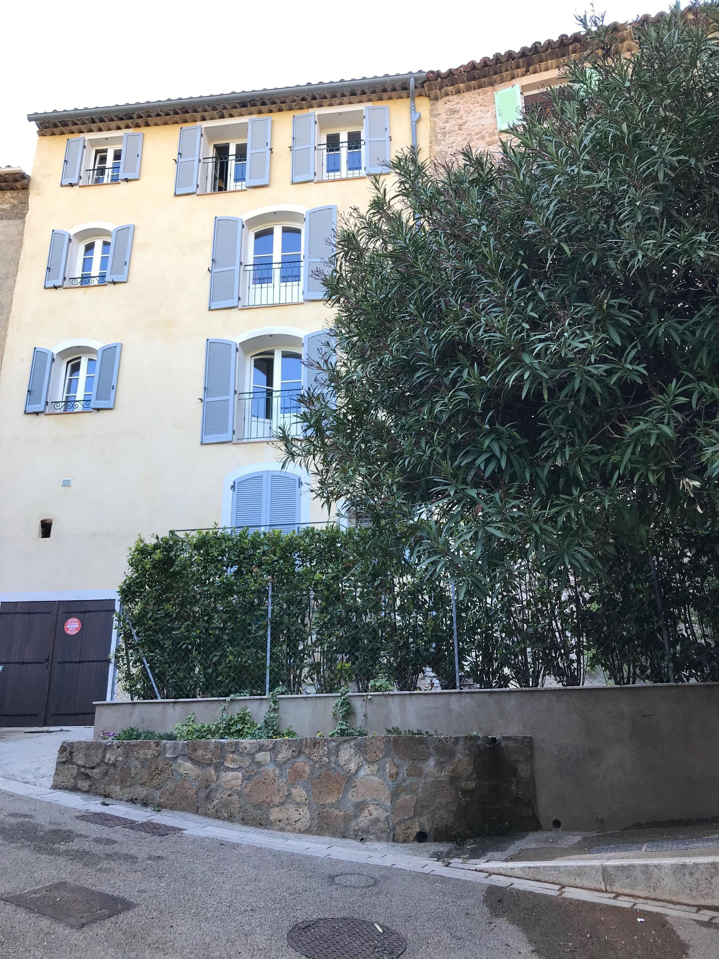 Un edificio de varios pisos con contraventanas azules, un muro de piedra y una reja de metal.