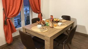 A dining table set with breakfast items, including bread, fruit, and juice, in a room with wooden flooring and red curtains. - Rigoletto Massena hyper center, 5 min beaches (Nice)