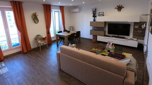 A living room with a sofa, a dining table, and a TV. - Rigoletto Massena hyper center, 5 min beaches (Nice)