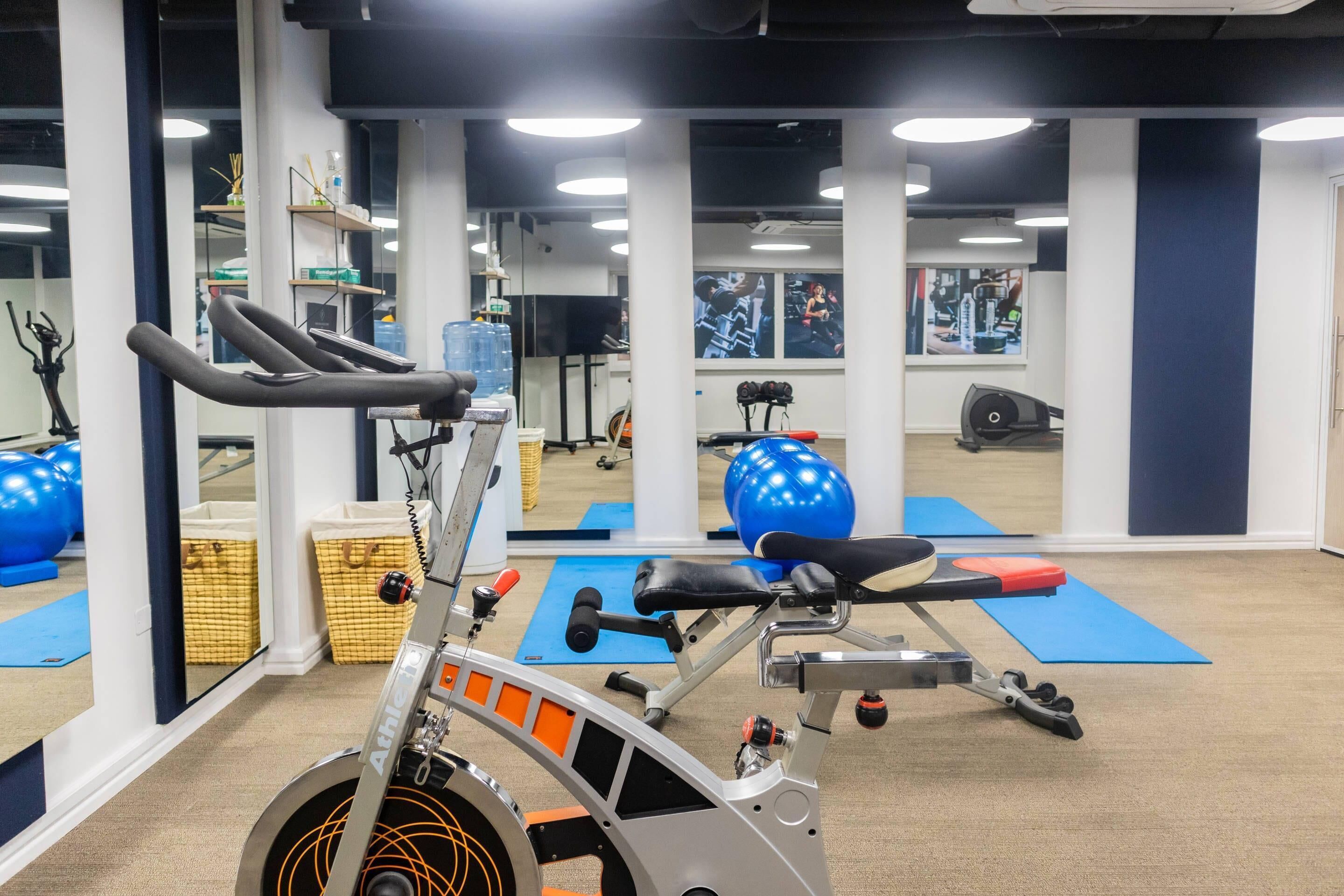 A stationary bike, exercise balls, and a treadmill in a gym with mirrors and blue mats.