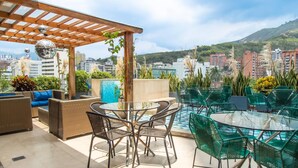 Un patio en la azotea con mobiliario de mimbre, una mesa de vidrio y una pérgola con bolas de discoteca colgantes.