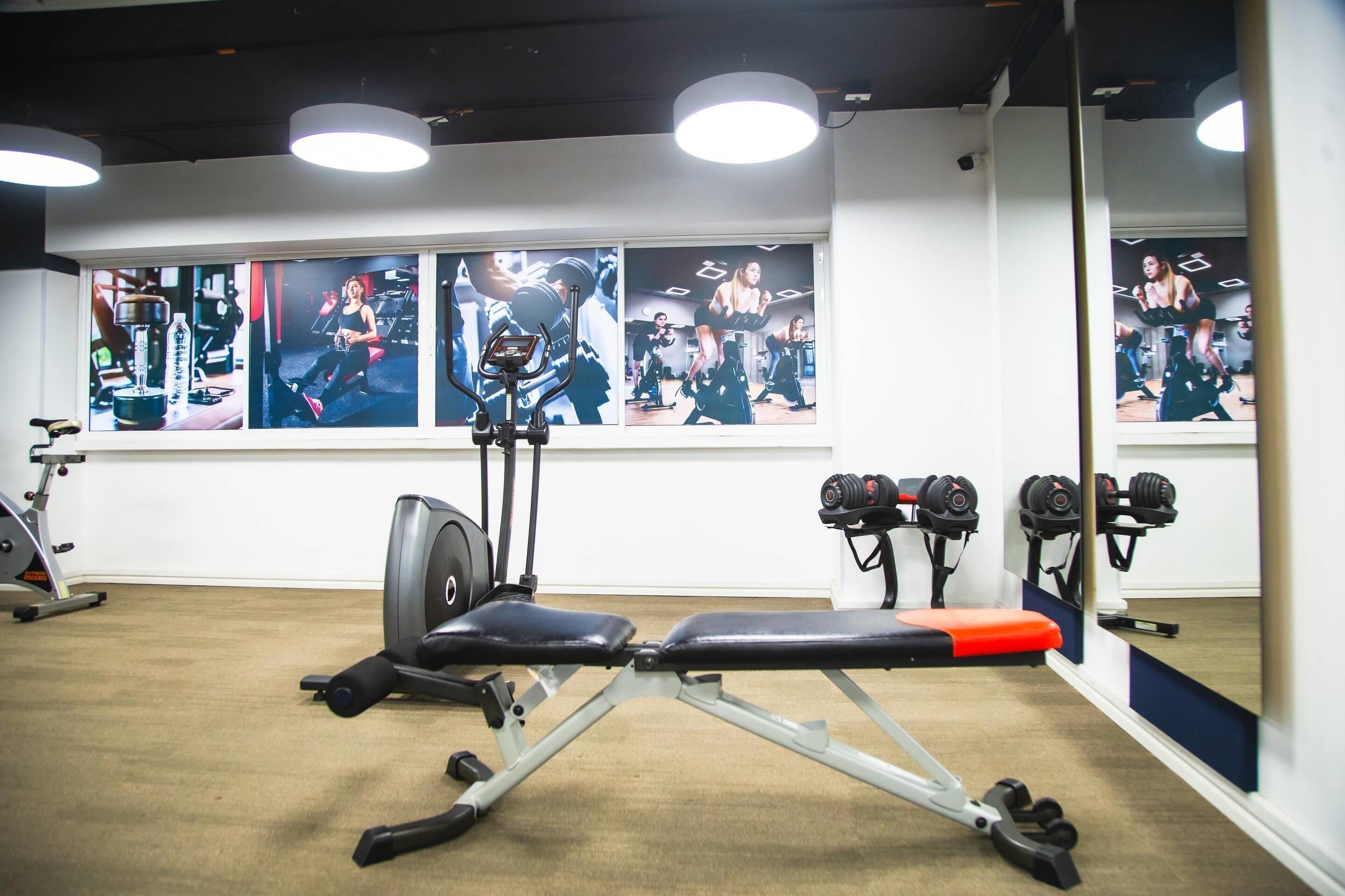 A gym with exercise equipment, a bench, and a wall with fitness posters.