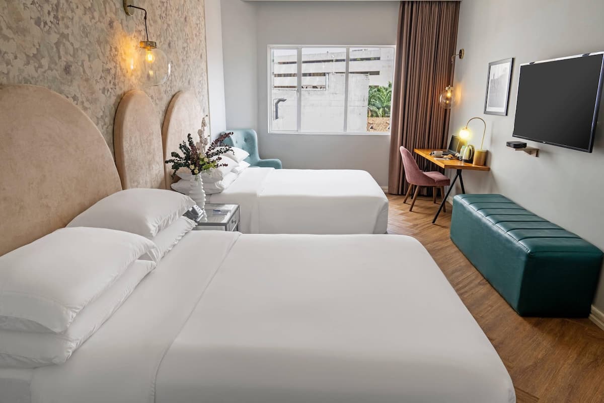 A hotel room with two beds, a desk with a chair, a TV, and a window with curtains.