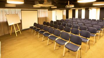 A conference room with rows of chairs, a whiteboard, and a projector screen.