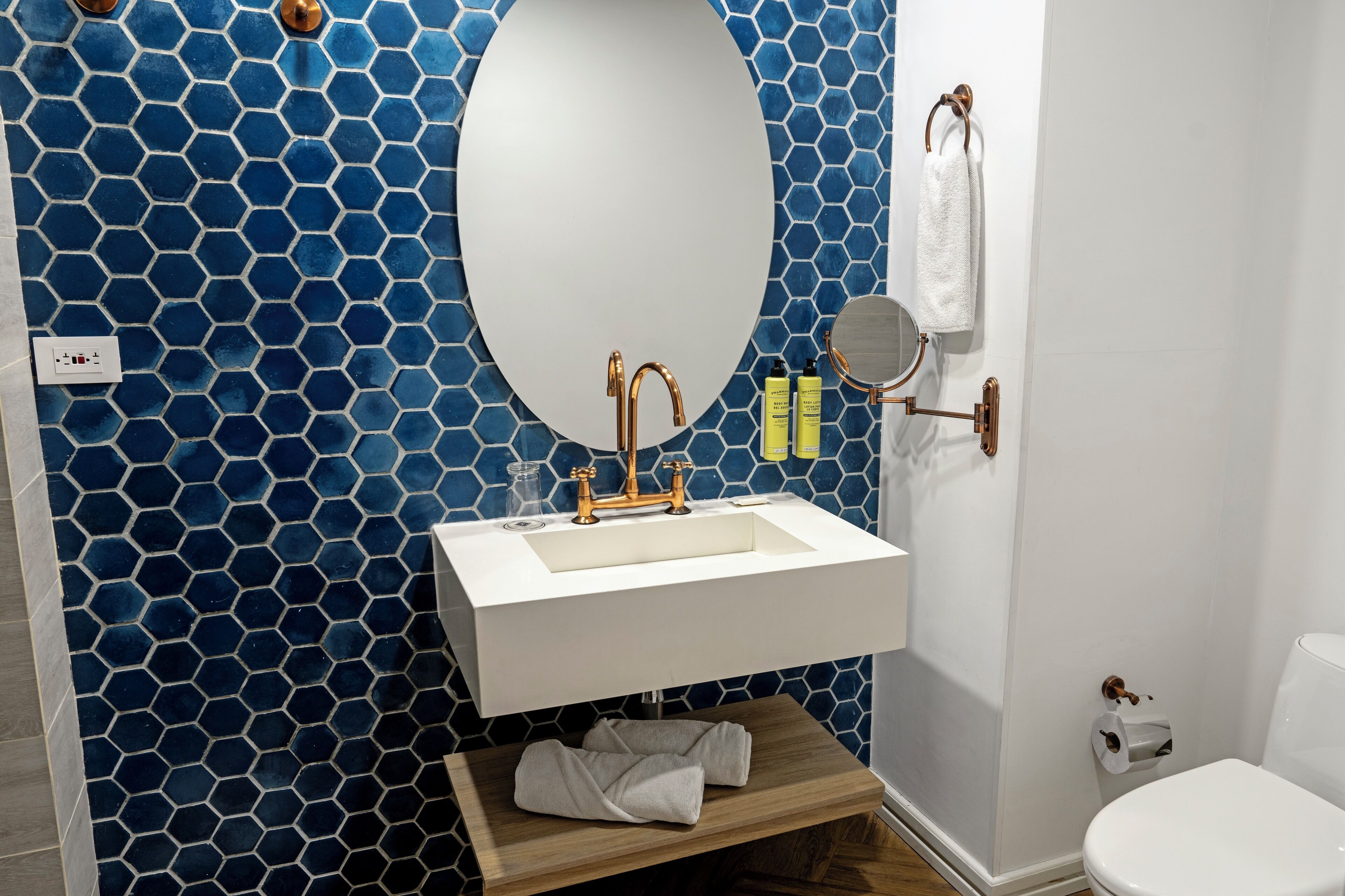 A bathroom with a white sink, a round mirror, and a blue hexagonal tile wall.