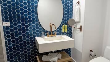 A bathroom with a white sink, a round mirror, and a blue hexagonal tile wall.