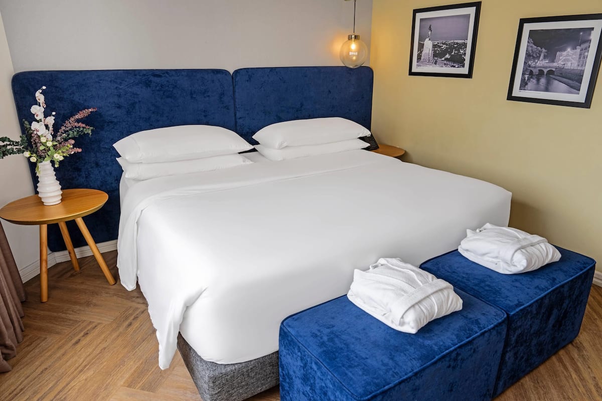 A double bed with white linens, a blue headboard, and a bedside table with a vase of flowers.