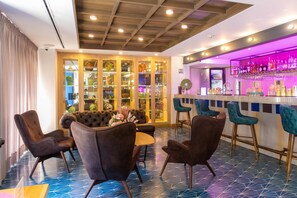 A bar area with stools and a bar counter, a seating area with a sofa and chairs, and a display of glassware. - Faranda Collection Cali, a member of Radisson Individuals (Cali)