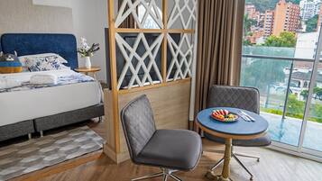 A hotel room with a bed, a desk, and a view of the city.