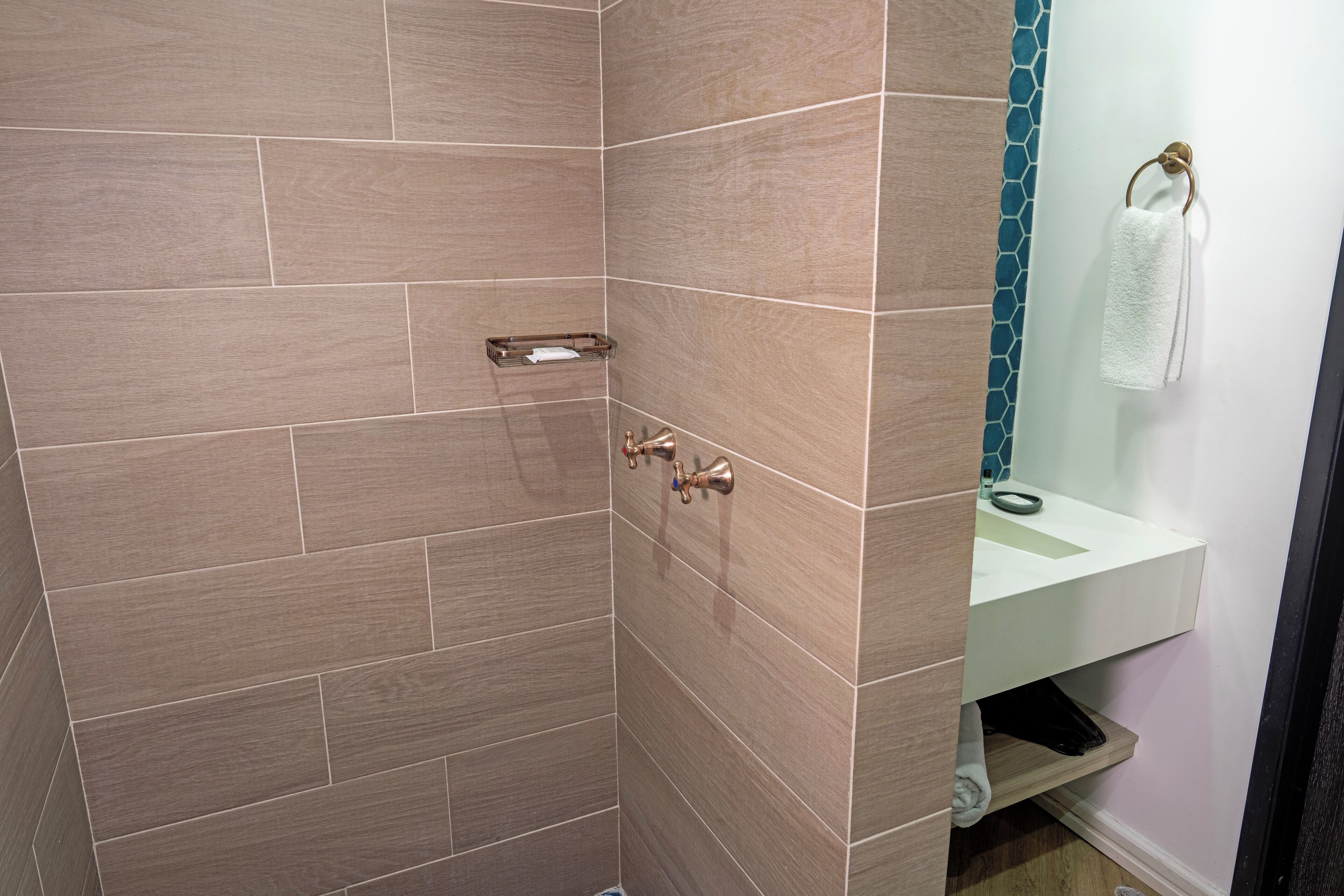 A bathroom with wooden tiles, a glass shower enclosure, a white sink, and a towel rack.