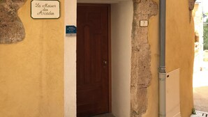 Ein Eingang mit einer Holztür, einem Schild mit der Aufschrift 'La Maison des Arcades' und einem kleinen Fenster mit der Nummer 7 darüber.