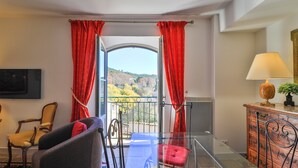 Ein Zimmer mit Balkon, einem Sessel, einer Couch, einer Lampe und Blick ins Freie.