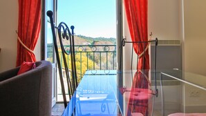 Ein Balkon mit Blick auf eine grüne Landschaft, einem Metallgeländer und einem Glastisch.