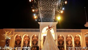 A grand hall with a long, flowing white gown on the floor, clear glass tables, and chairs arranged for an event. - Kalaa Resort (Arnoun)