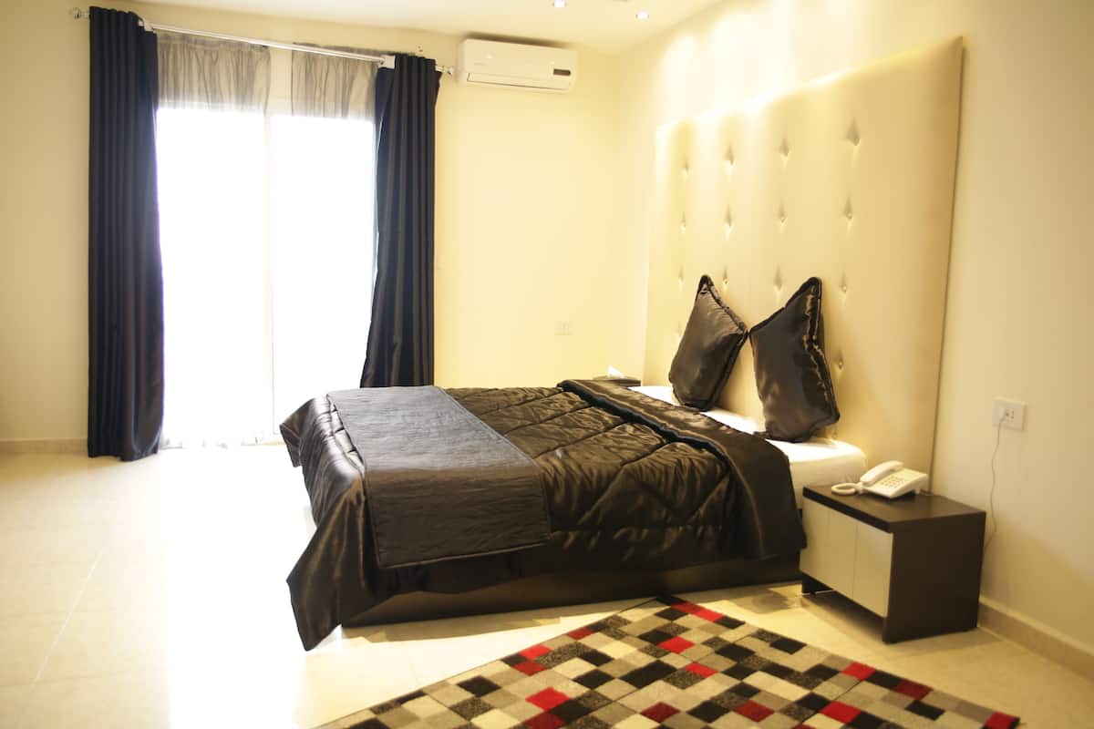 Un dormitorio con una cama grande, una mesita de noche con teléfono y una ventana con cortinas.
