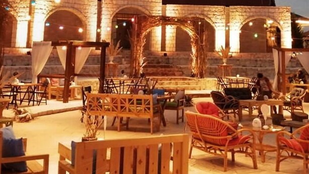 An outdoor seating area with wooden furniture and stone arches in the background. - Kalaa Resort (Arnoun)