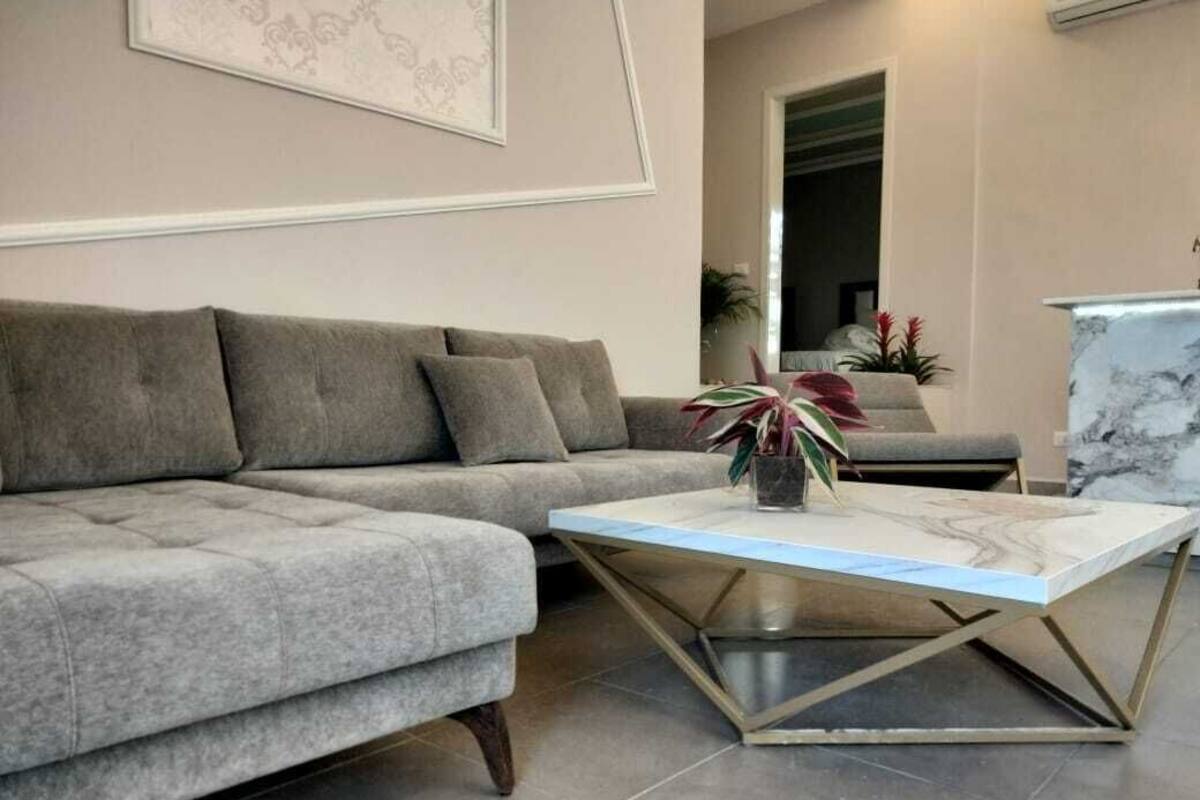 Una sala de estar moderna con un sofá seccional gris, una mesa de centro de mármol y una obra de arte enmarcada en la pared.