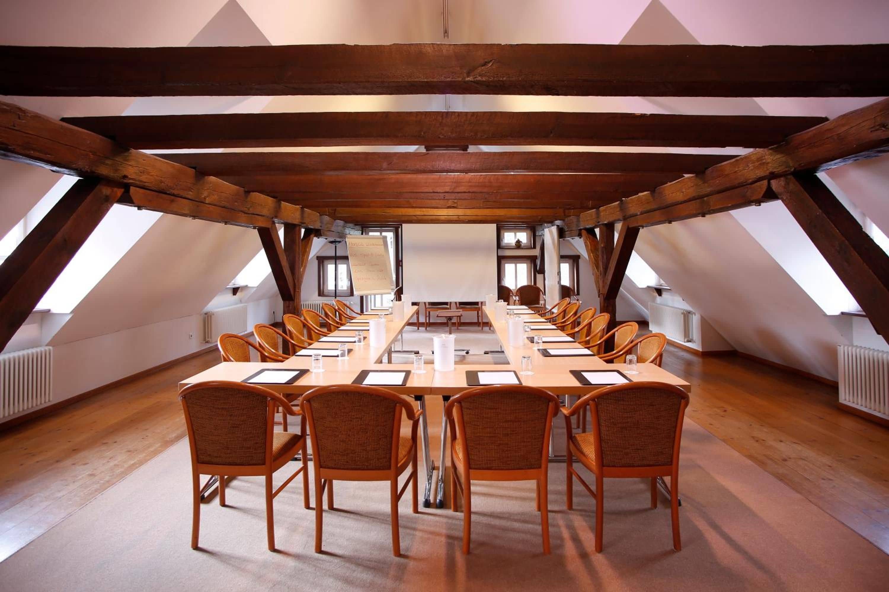 Una sala de conferencias con una larga mesa, varias sillas y un techo alto con vigas de madera a la vista.