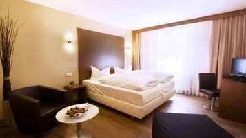 Ein Hotelzimmer mit einem Bett, einem kleinen runden Tisch mit einer Obstschale, einer Couch, einem Fernseher und einem großen Fenster mit Vorhängen.