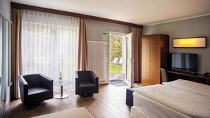 A hotel room with a bed, two armchairs, a small table, a television, and a view of the outdoors through a sliding door. - Springbach-Mühle Belzig (Bad Belzig)