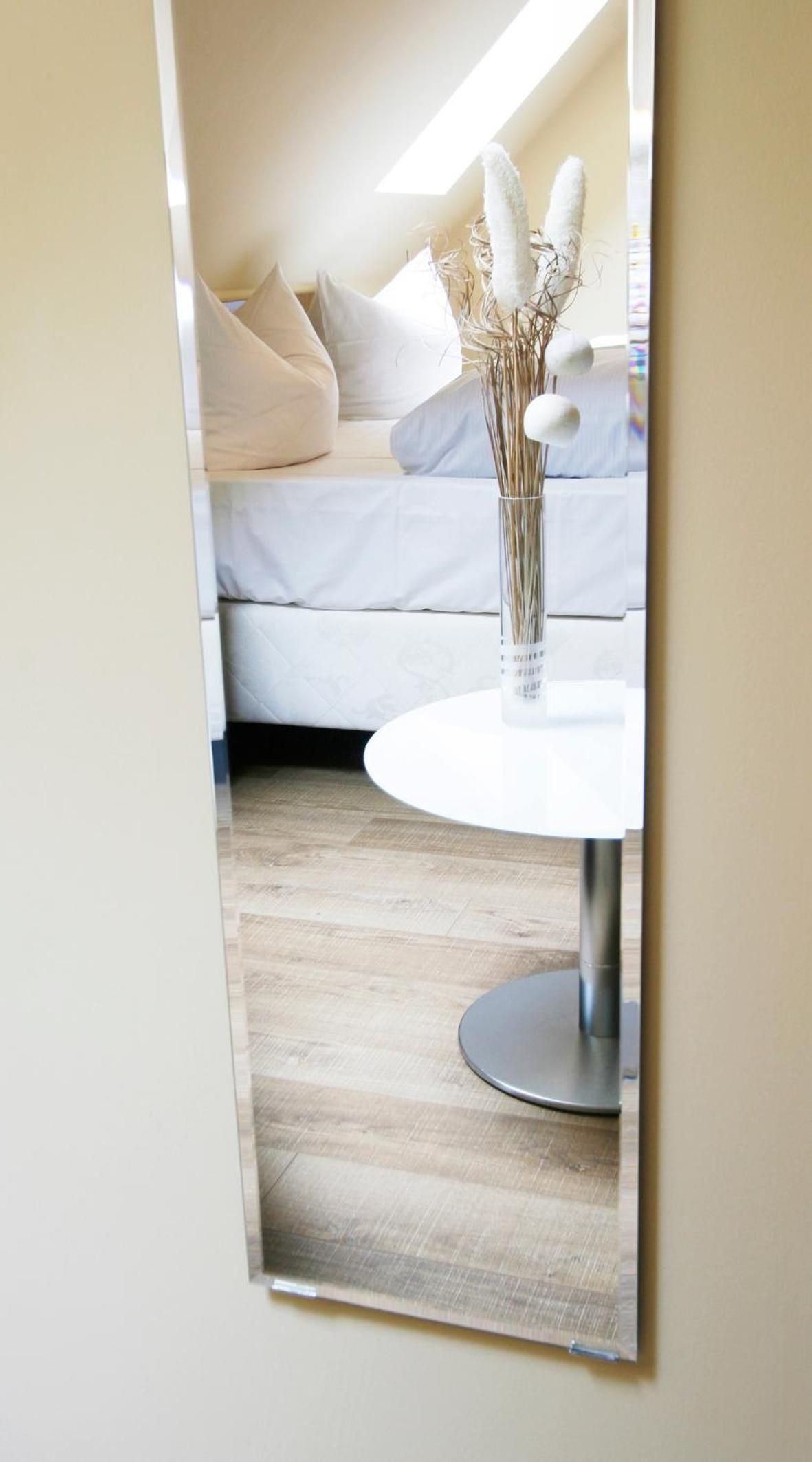 A room with a white round table, a vase with dried plants, and a white sofa with cushions.