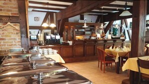 A buffet setup with stainless steel chafing dishes, wooden bar counters, and a tiled floor. - Springbach-Mühle Belzig (Bad Belzig)