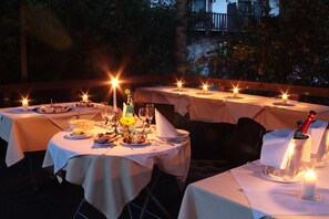 An outdoor dining area with tables set for a meal, candles, and a bottle of champagne.