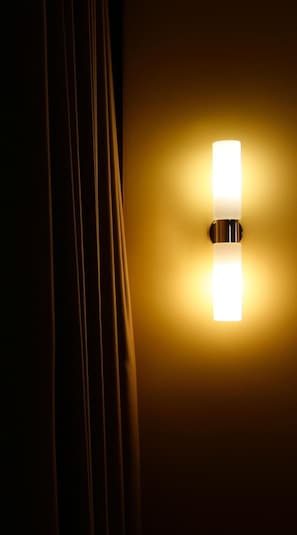 A wall-mounted light fixture with a rectangular shape and a metallic base, casting a warm glow on the wall.