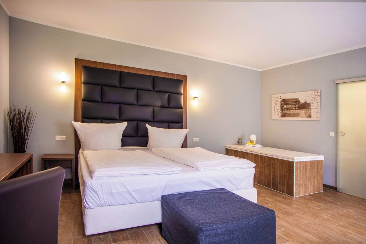 Una habitación de hotel moderna con una cama grande, cabecera de madera, una mesita de noche, un escritorio y un pequeño rincón de descanso.
