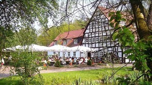 A traditional half-timbered building with a red roof, surrounded by a pond and greenery. - Springbach-Mühle Belzig (Bad Belzig)