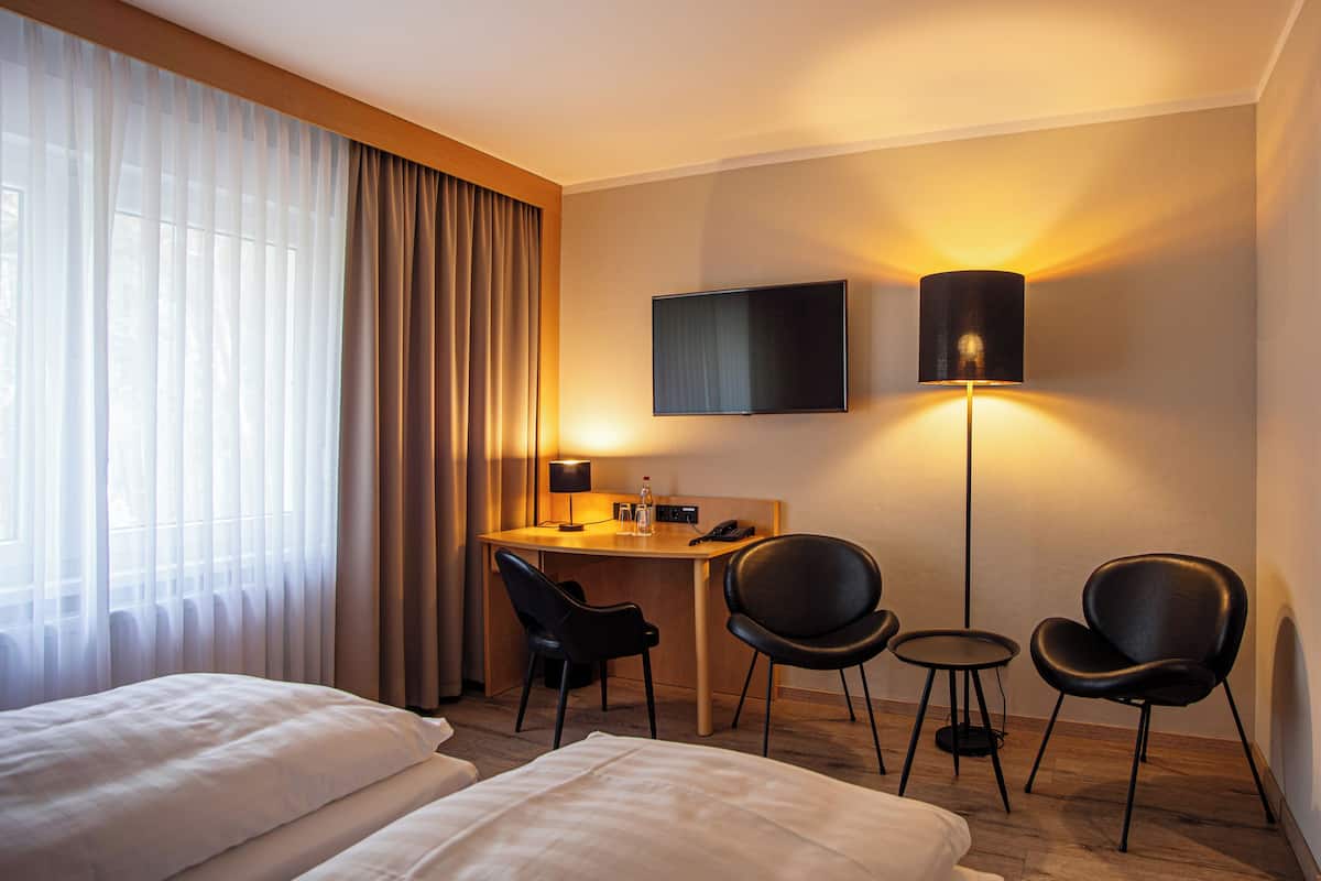 Una habitación de hotel con una cama, un escritorio con silla, un televisor y una lámpara.