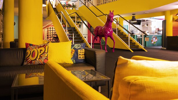 A vibrant interior with yellow walls, a staircase, and a colorful couch with a glass table. - The Fox Hotel (Ponce)