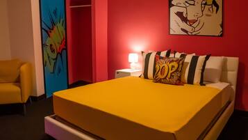 A hotel room with a yellow bed, a red wall, a blue door, and a yellow armchair.