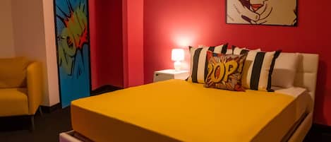 A hotel room with a yellow bed, a red wall, a blue door, and a yellow armchair.