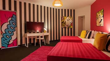 A room with striped walls, a bed with red bedding, a desk with a chair, a television, and artwork on the walls.