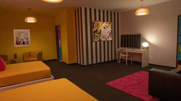 Habitación de hotel con dos camas, un escritorio y una silla. Hay dos lámparas colgantes y un cuadro grande en la pared.