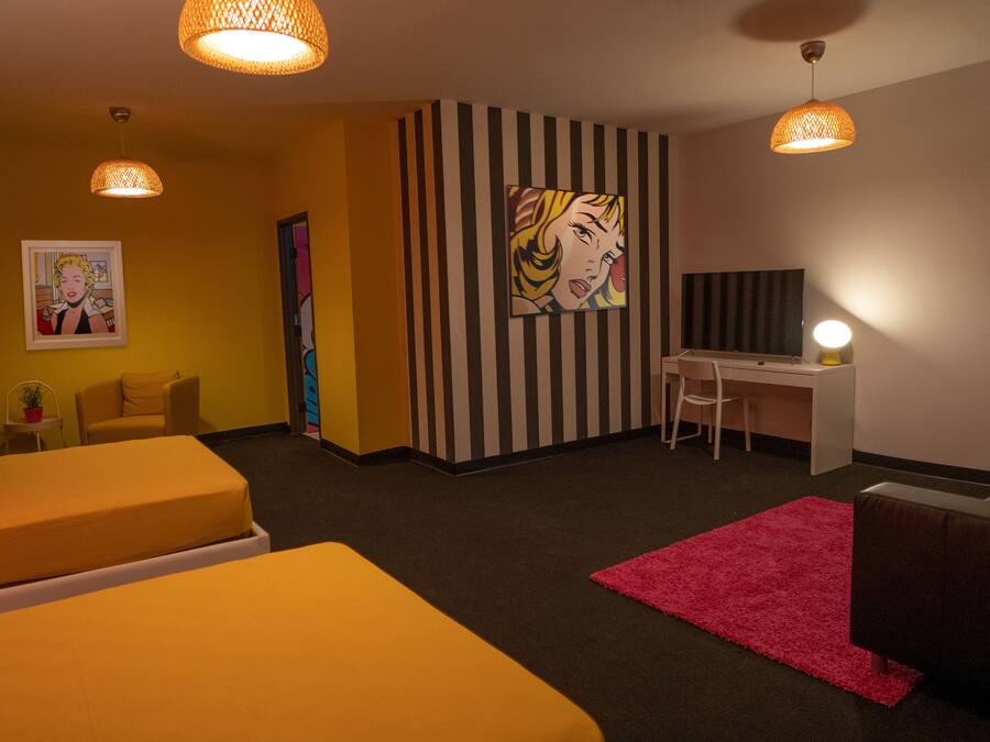 Habitación de hotel con dos camas, un escritorio y una silla. Hay dos lámparas colgantes y un cuadro grande en la pared.