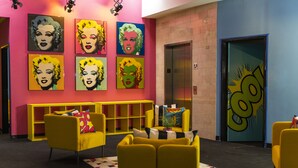 A lobby with vibrant artwork, yellow seating, and a modern elevator. - The Fox Hotel (Ponce)